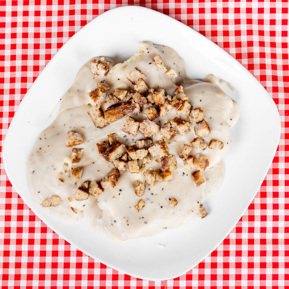 Creamy white-sauce pasta topped with toasted breadcrumbs on a white plate over a red-and-white checkered tablecloth.