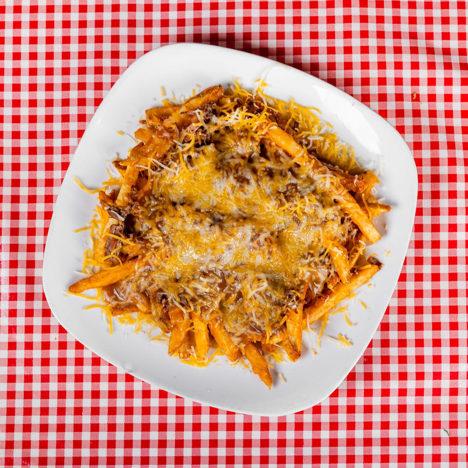 Plate of French fries topped with seasoned ground beef and melted shredded cheese on a red-and-white checkered tablecloth.
