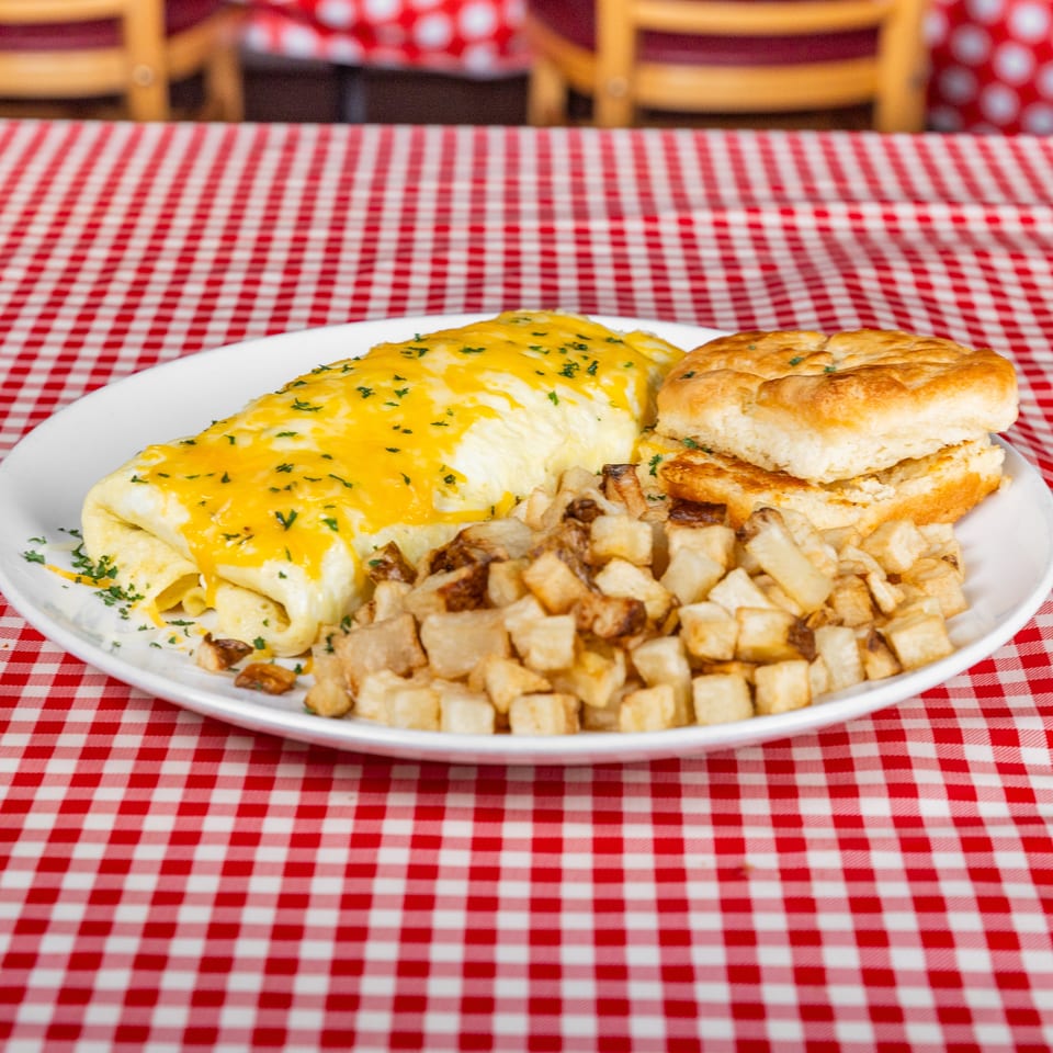 Cheesy herb-topped omelet served with biscuits and golden breakfast potatoes on a red-and-white checkered tablecloth.