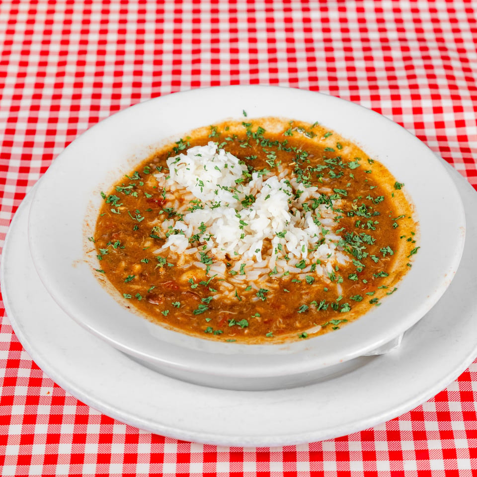 White rice topped with parsley sits in a savory brown sauce on a white plate over a red-and-white checkered tablecloth.