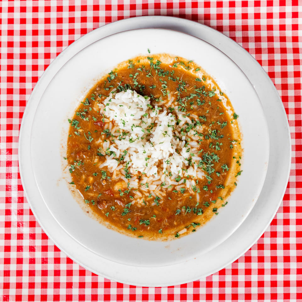White rice surrounded by rich brown sauce and chopped herbs on a plate atop a red-and-white checkered tablecloth.