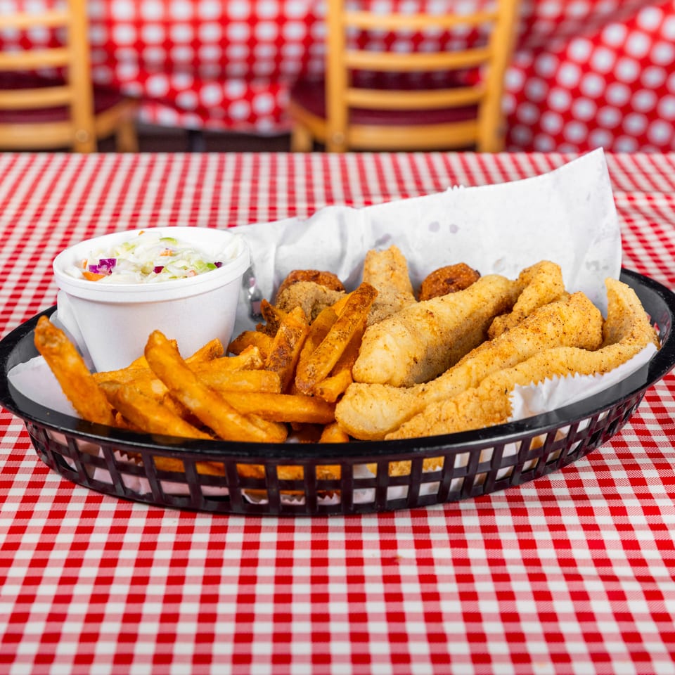 Basket of fried fish, shrimp, and fries with coleslaw on a red-and-white checkered restaurant table.