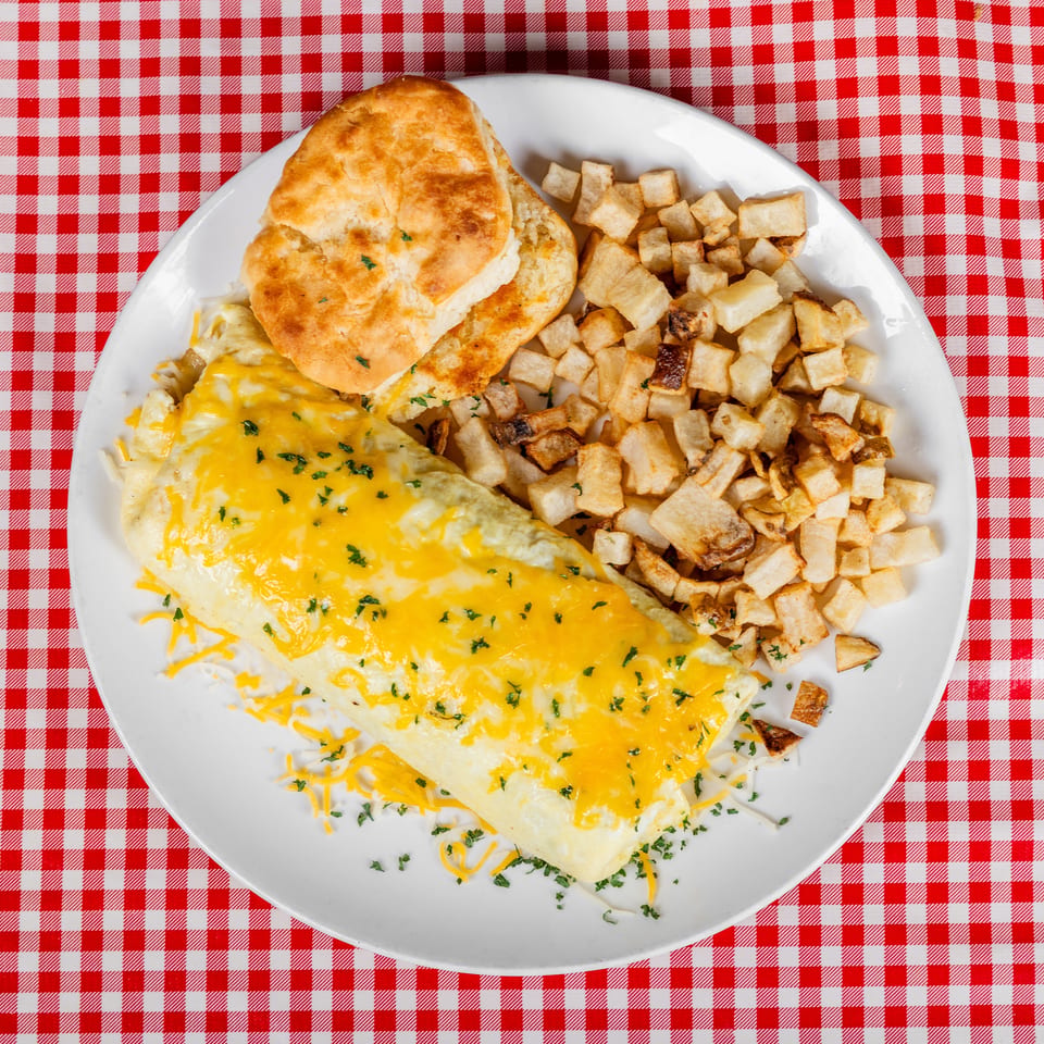 Cheesy folded omelet with herbs, home fries, and biscuits served on a white plate over a red-and-white checkered tablecloth.
