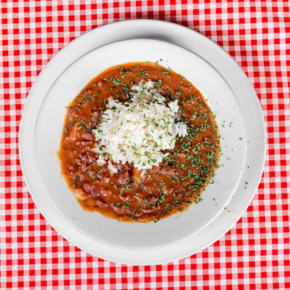 White rice surrounded by red bean stew and garnished with parsley on a white plate atop a red-and-white checkered tablecloth.