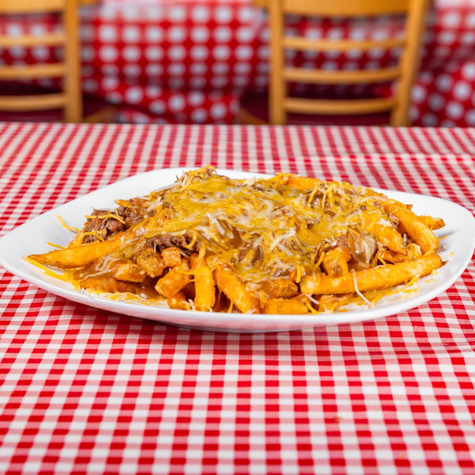 Loaded fries topped with shredded beef, melted cheese, and sauce on a white plate over a red-and-white checkered tablecloth.